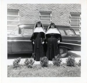 black and white photo of two sisters in habit standing in front of car