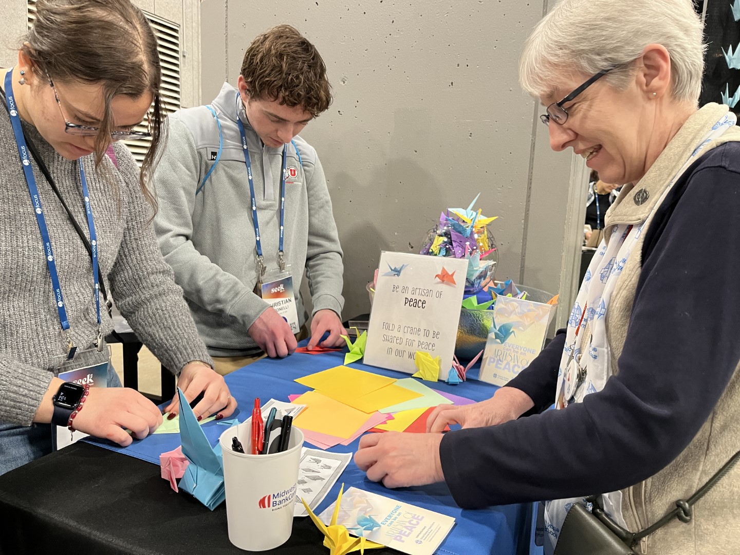 Sister Jill Laszewski helps two young adults fold origami cranes for peace at the SEEK24 conference in St. Louis, January 1-5, 2024.